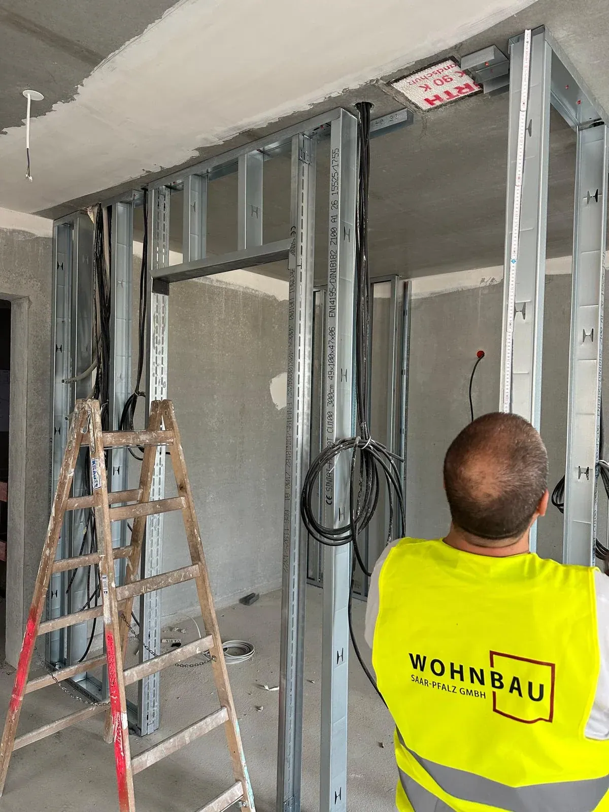 Monteur in Wohnbau-Saar-Pfalz-Warnweste beim Ausrichten des Trockenbau-Ständerwerks