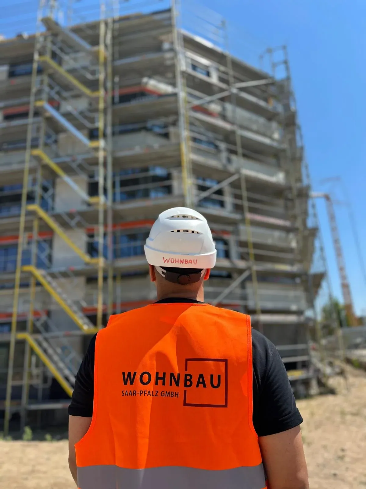 Mitarbeiter in Wohnbau-Saar-Pfalz-Warnweste vor einem eingerüsteten Gebäude